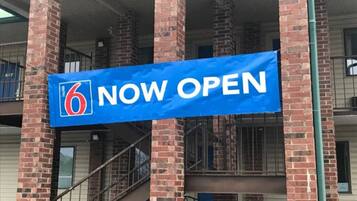 Un cartellone blu con il numero 6 e la scritta 'NOW OPEN', che segnala l'apertura di un motel.