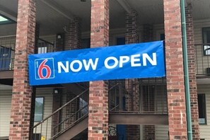 Een blauwe banner met het cijfer 6 en de tekst 'NU OPEN', wat aangeeft dat een hotel of motel operationeel is.