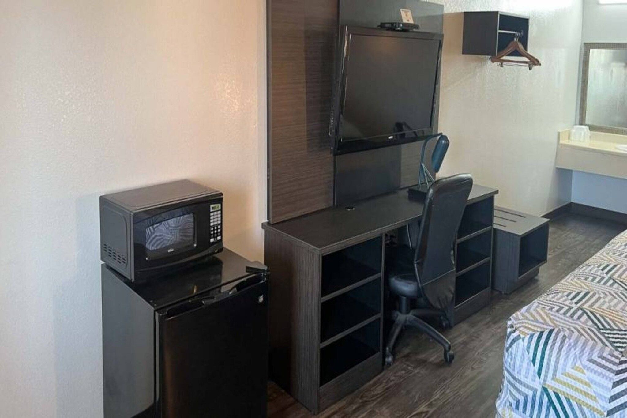 A compact hotel room with a kitchenette, a television, a bed, and a desk.