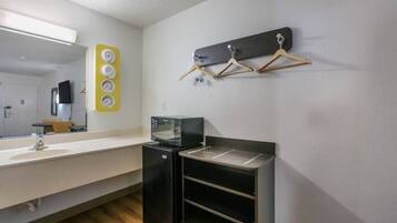 Hotelværelse med tekøkken, vask, spejl og et vægmonteret hyldesæt med knager.