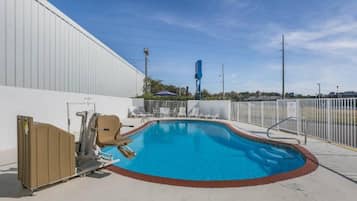 A swimming pool with a white fence, lounge chairs, and a portable toilet.