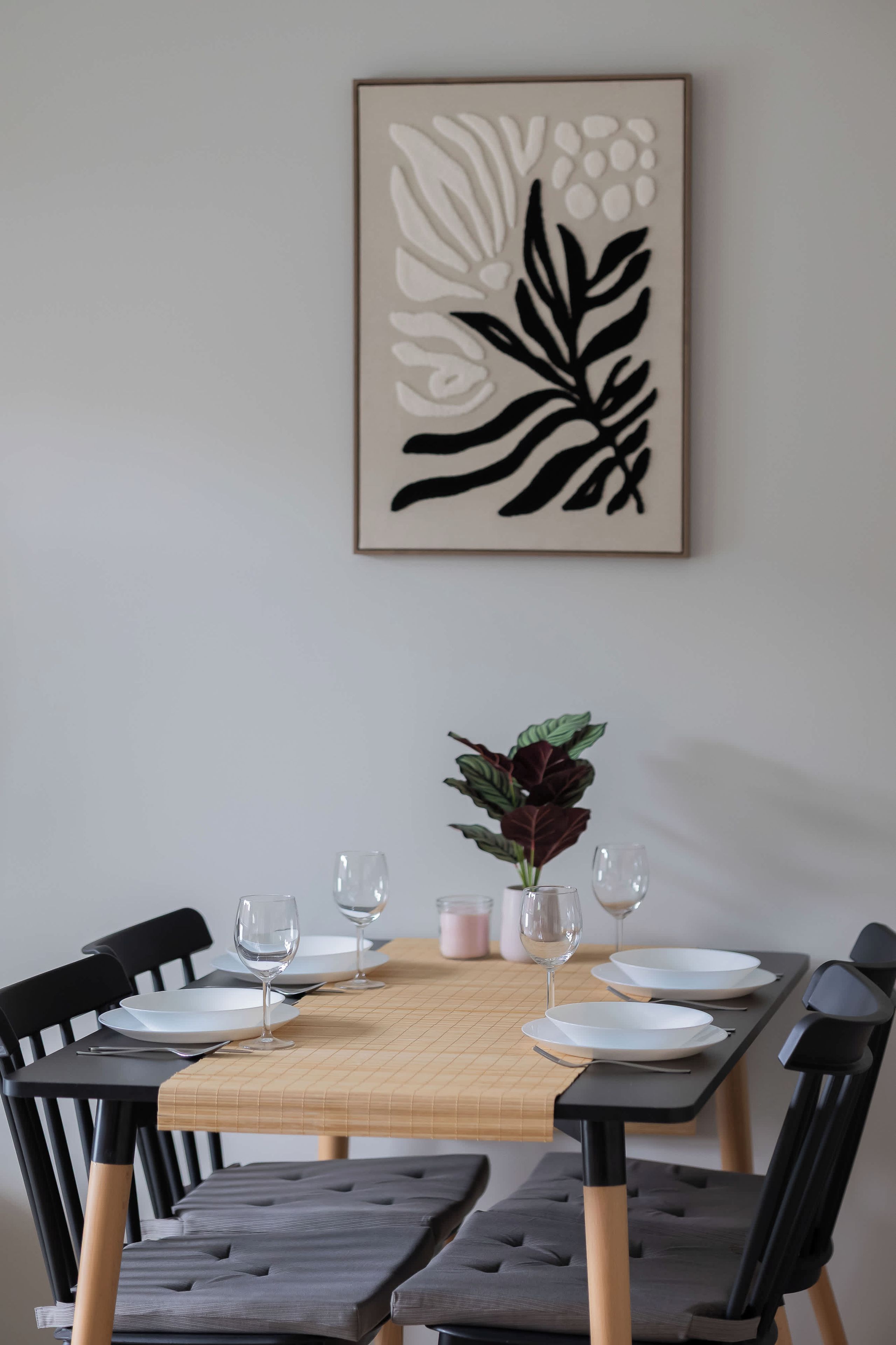 A dining table with chairs, a vase with a plant, and a framed artwork on the wall.