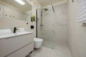 Une salle de bain moderne avec un meuble-lavabo blanc, des toilettes, une douche en verre et un porte-serviettes.