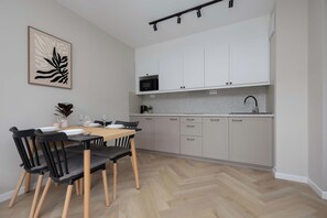 Une cuisine moderne avec des meubles blancs, un four à micro-ondes et un évier. On y trouve une table à manger avec des chaises, et une plante est accrochée au mur.
