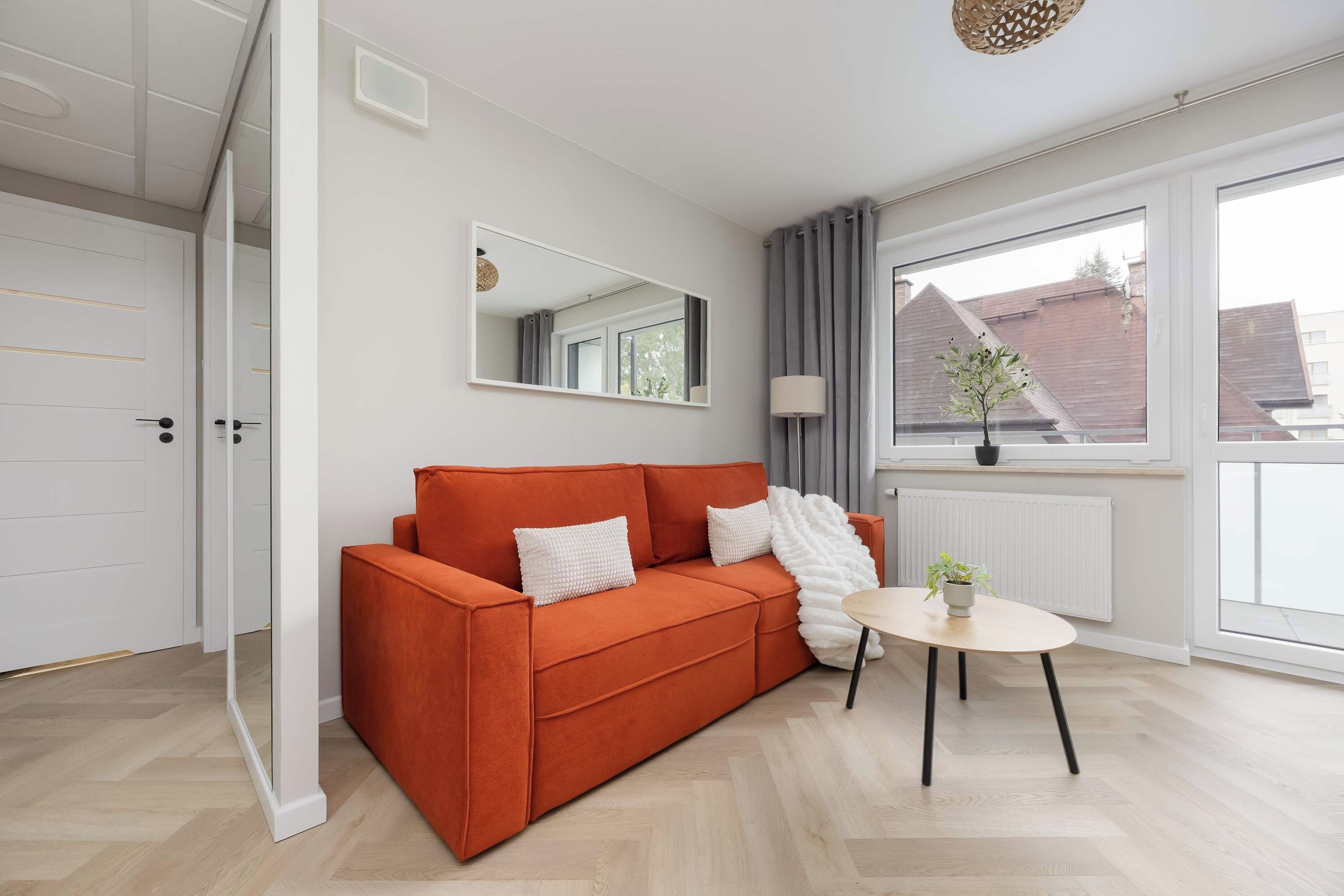 A modern living room with a sofa, a round table, a mirror, and a window with curtains.