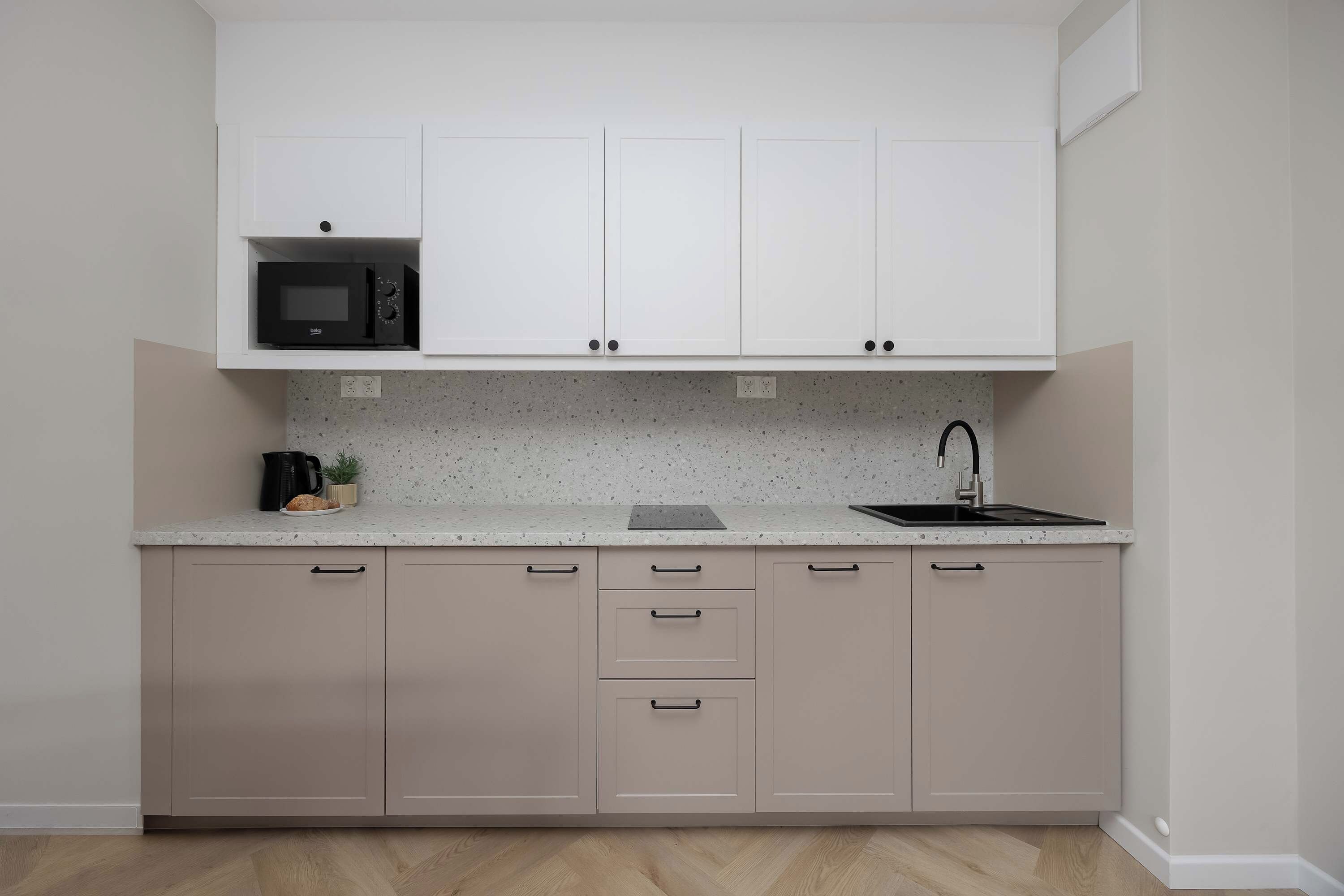 A modern kitchen with a built-in microwave, a sink, and a countertop with a speckled backsplash.