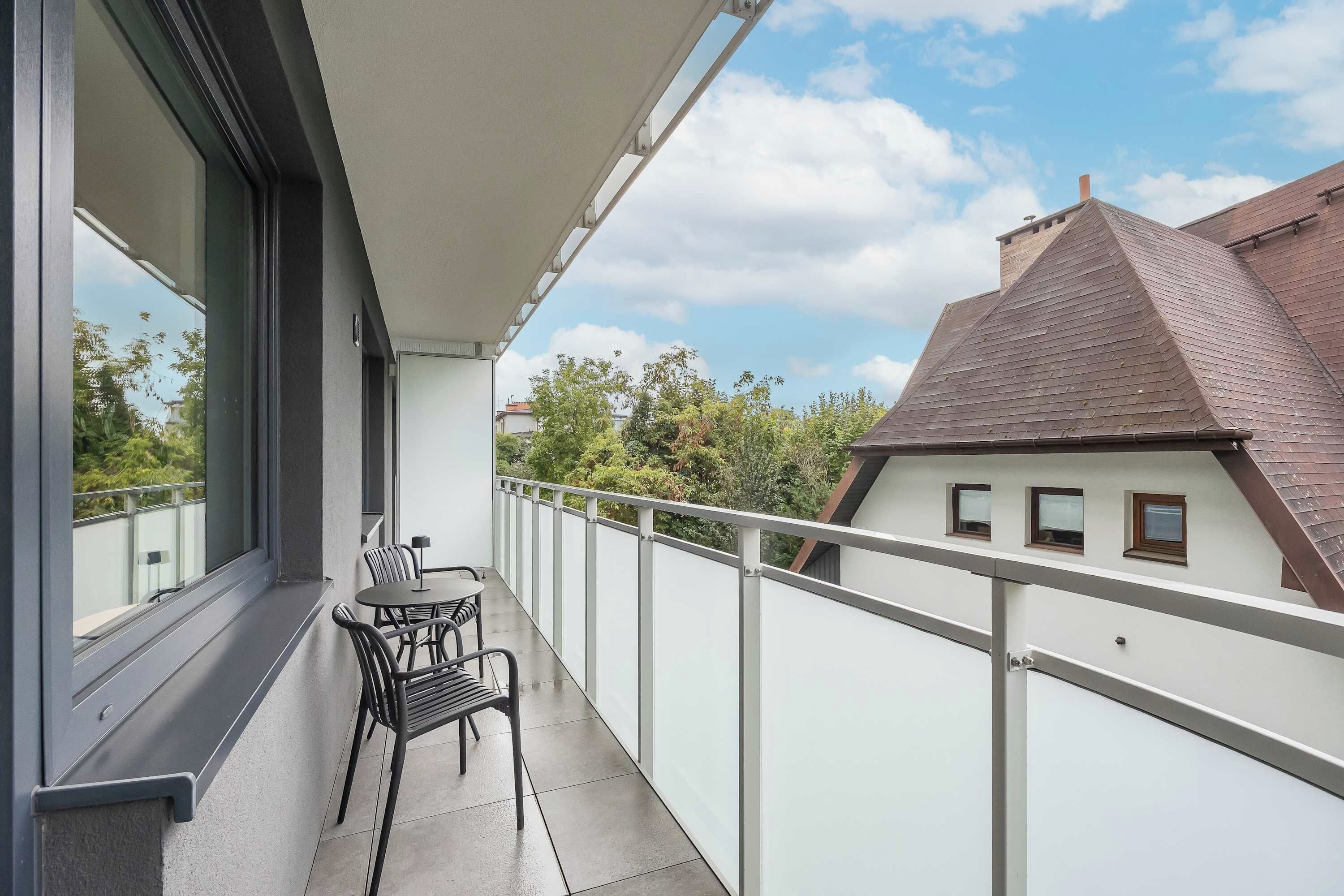 A balcony with a table and chairs, a white railing, and a view of a neighboring building.