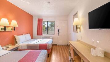 A hotel room with two beds, a desk, a chair, a TV, and a window with curtains.