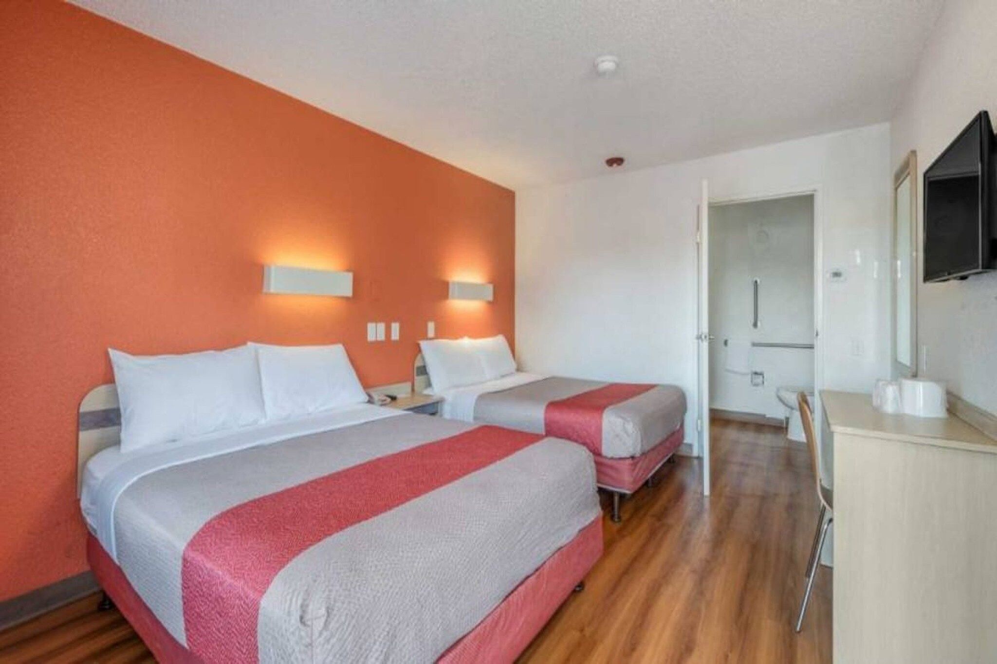 A hotel room with two beds, a desk, a mirror, and a door leading to a bathroom.