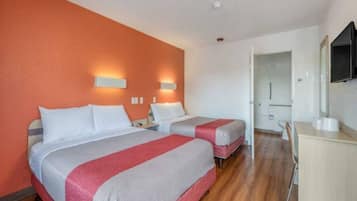 A hotel room with two beds, a desk, a mirror, and a door leading to a bathroom.