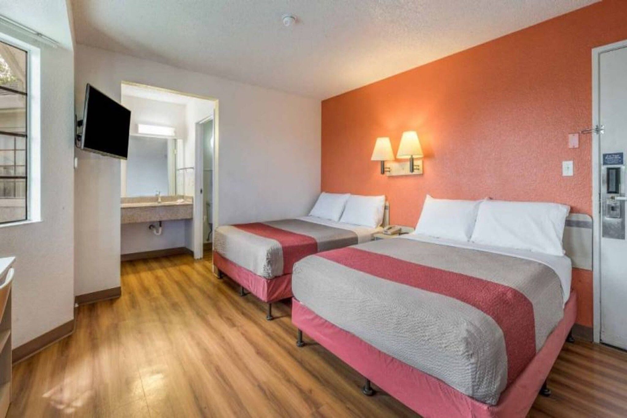 A hotel room with two beds, a television, a bathroom, and a wooden floor.