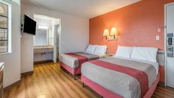 A hotel room with two beds, a television, a bathroom, and a wooden floor.