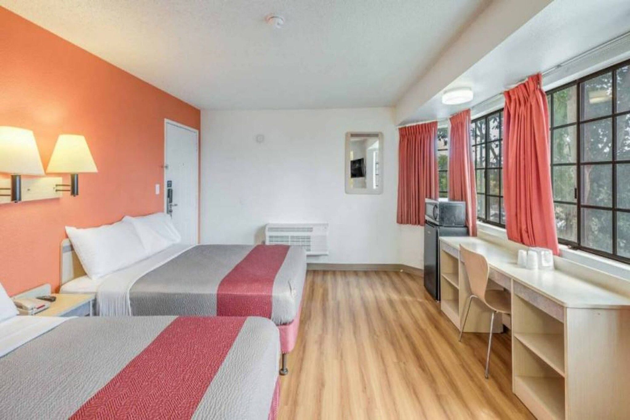 A hotel room with two beds, a desk, a chair, a TV, and a window with curtains.