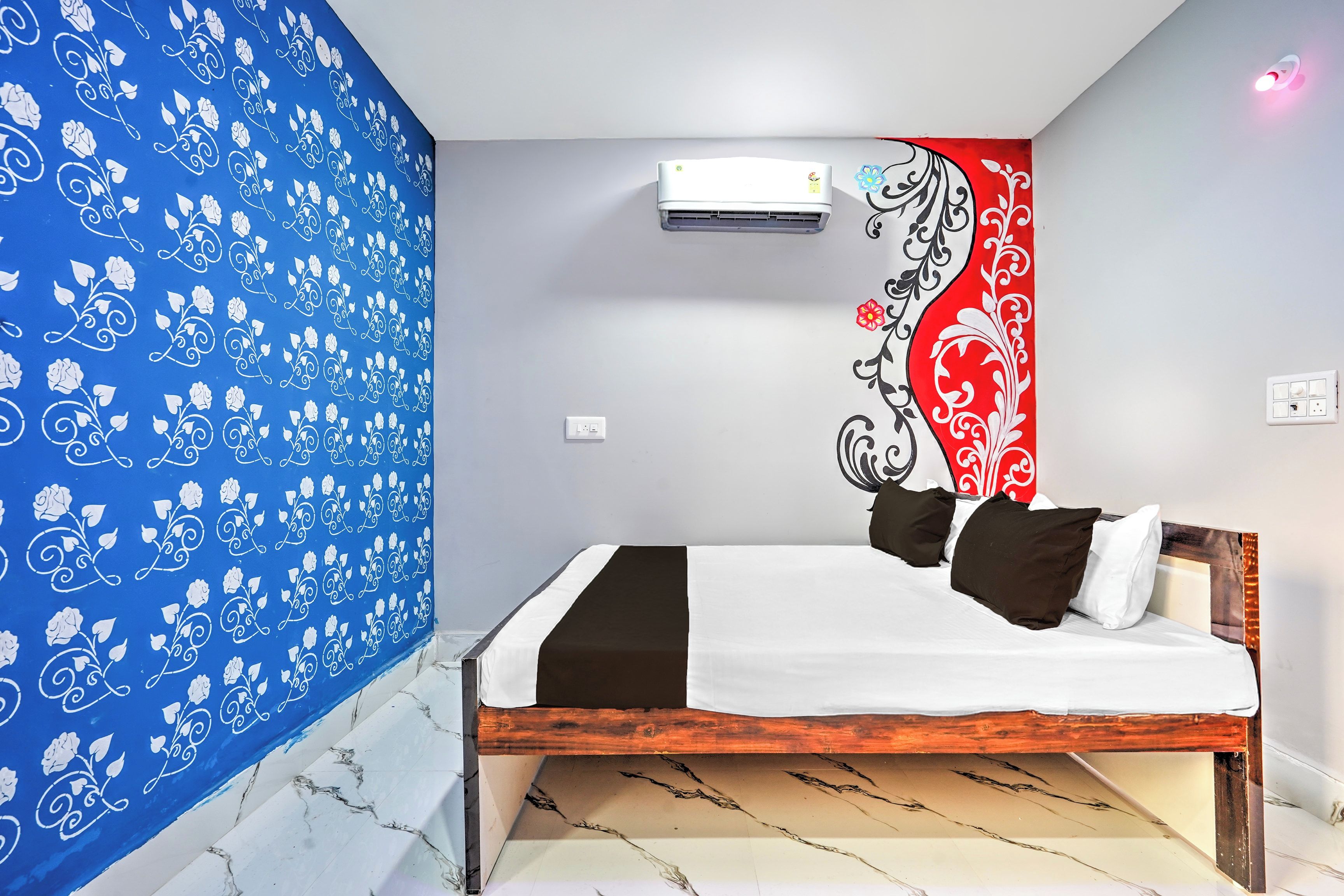 A bedroom with a bed, a wall with a floral pattern, an air conditioning unit, and a wall with a red and black design.