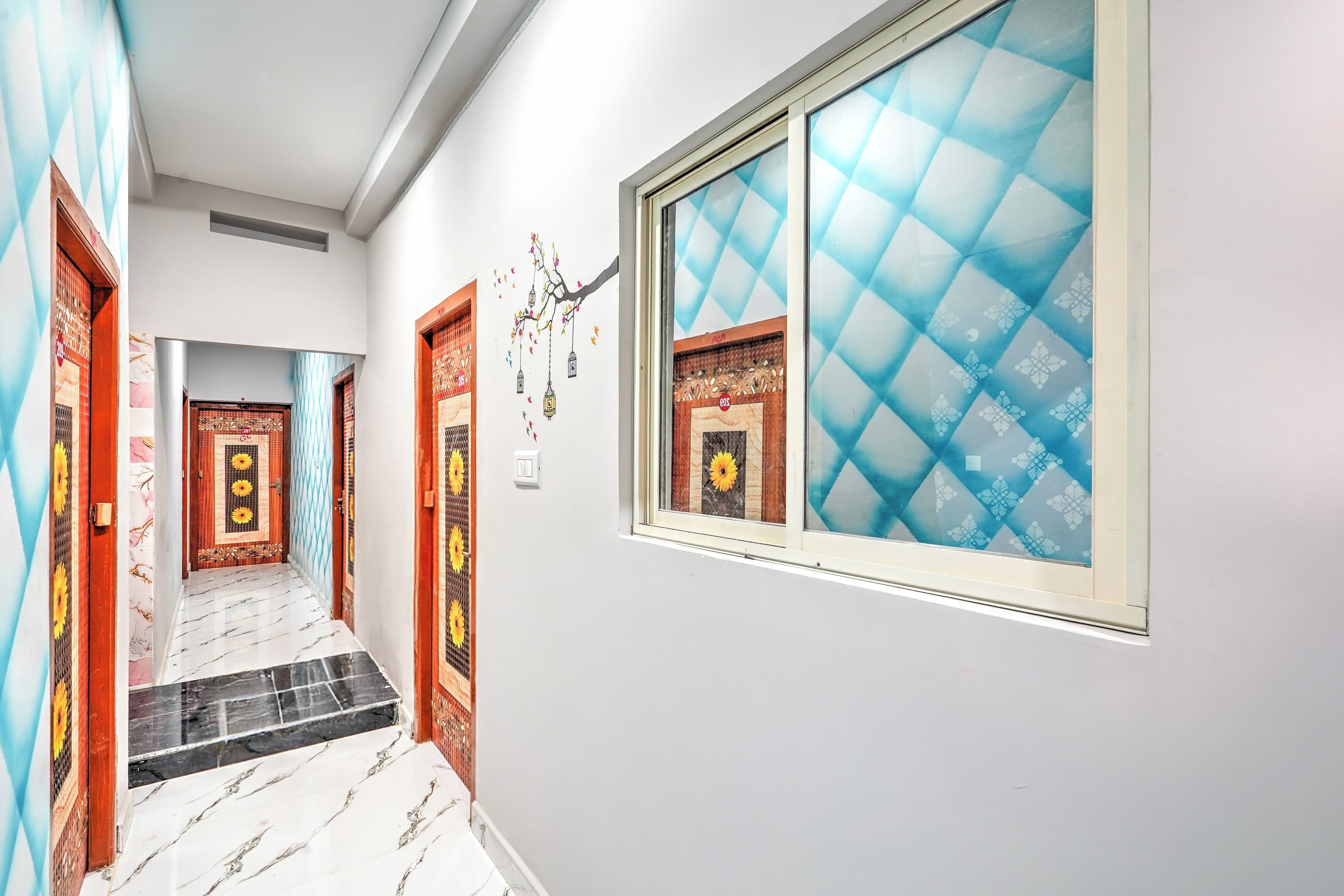 Un couloir avec des portes décorées de motifs, un sol carrelé et une fenêtre ornée d’un store bleu à motifs.
