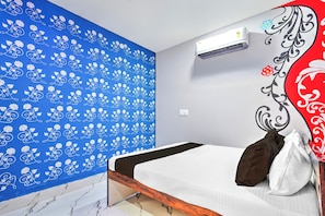 A bedroom with a bed, a blue patterned wall, an air conditioning unit, and a decorative wall panel.