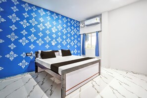 A modern bedroom with a bed, a blue patterned wall, an air conditioning unit, and a window with curtains.