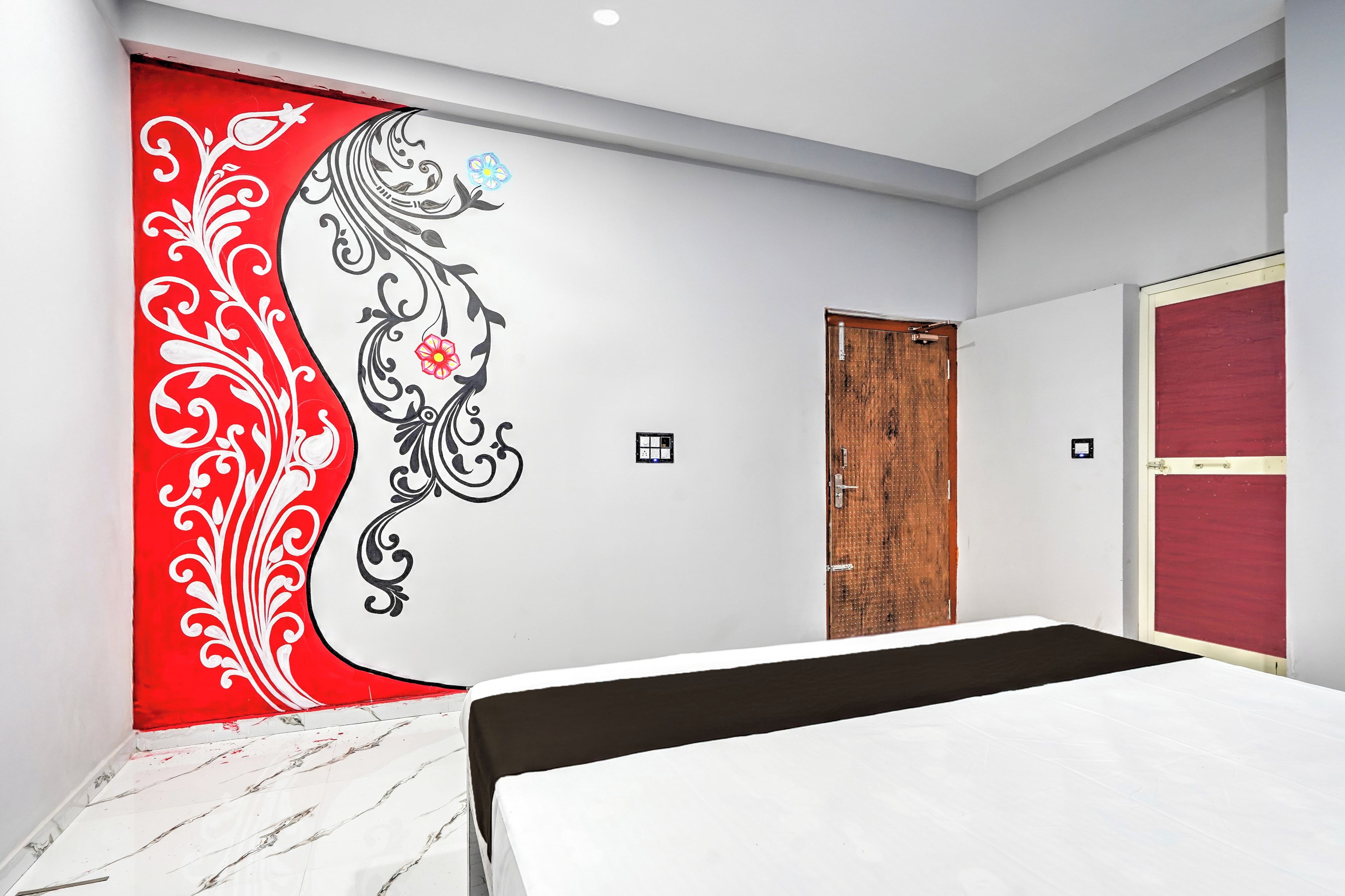 Un dormitorio con una cama, una puerta de madera y un diseño decorativo rojo y blanco en la pared.
