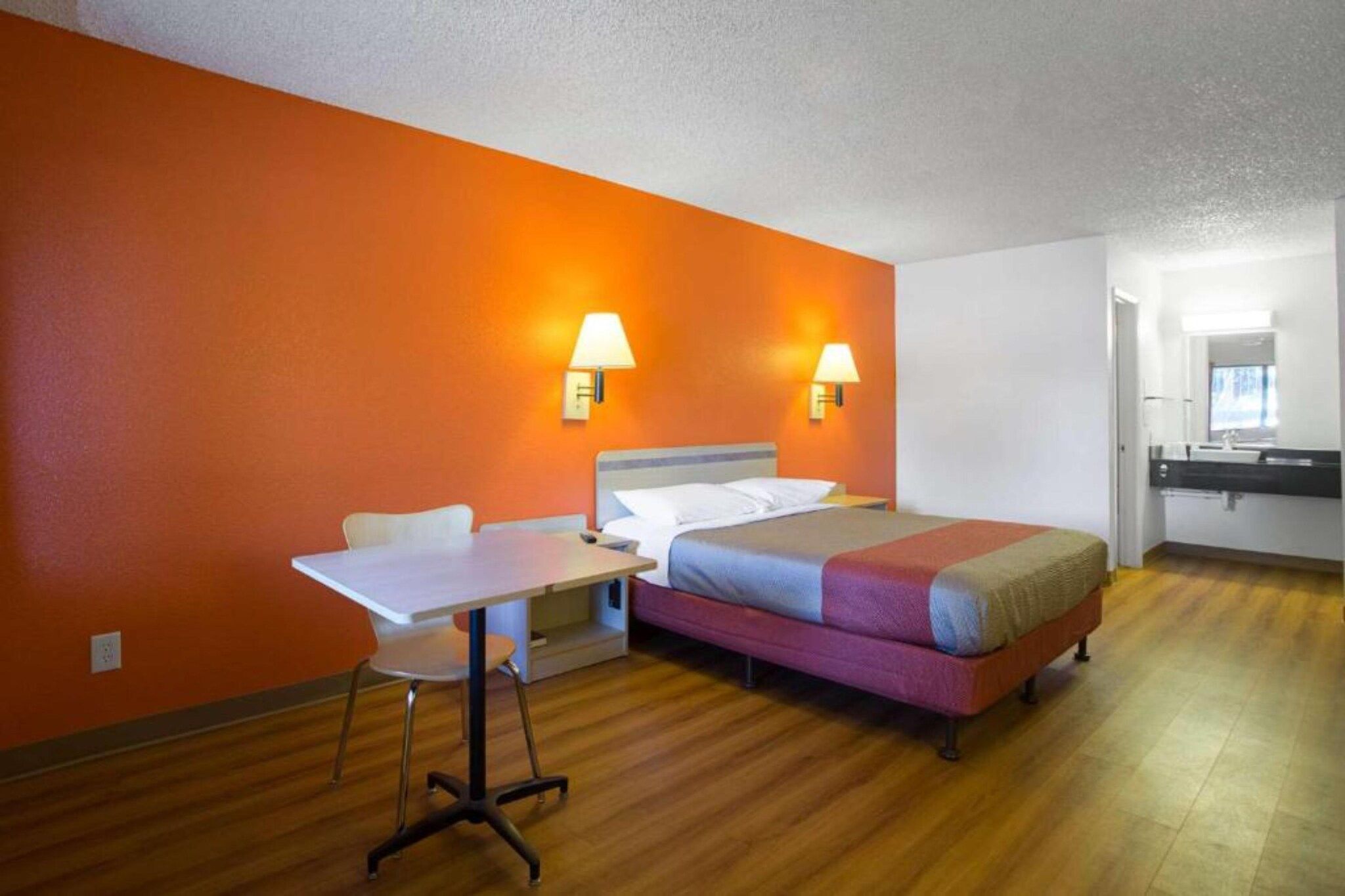 A hotel room with a bed, a desk, and two wall-mounted lamps.