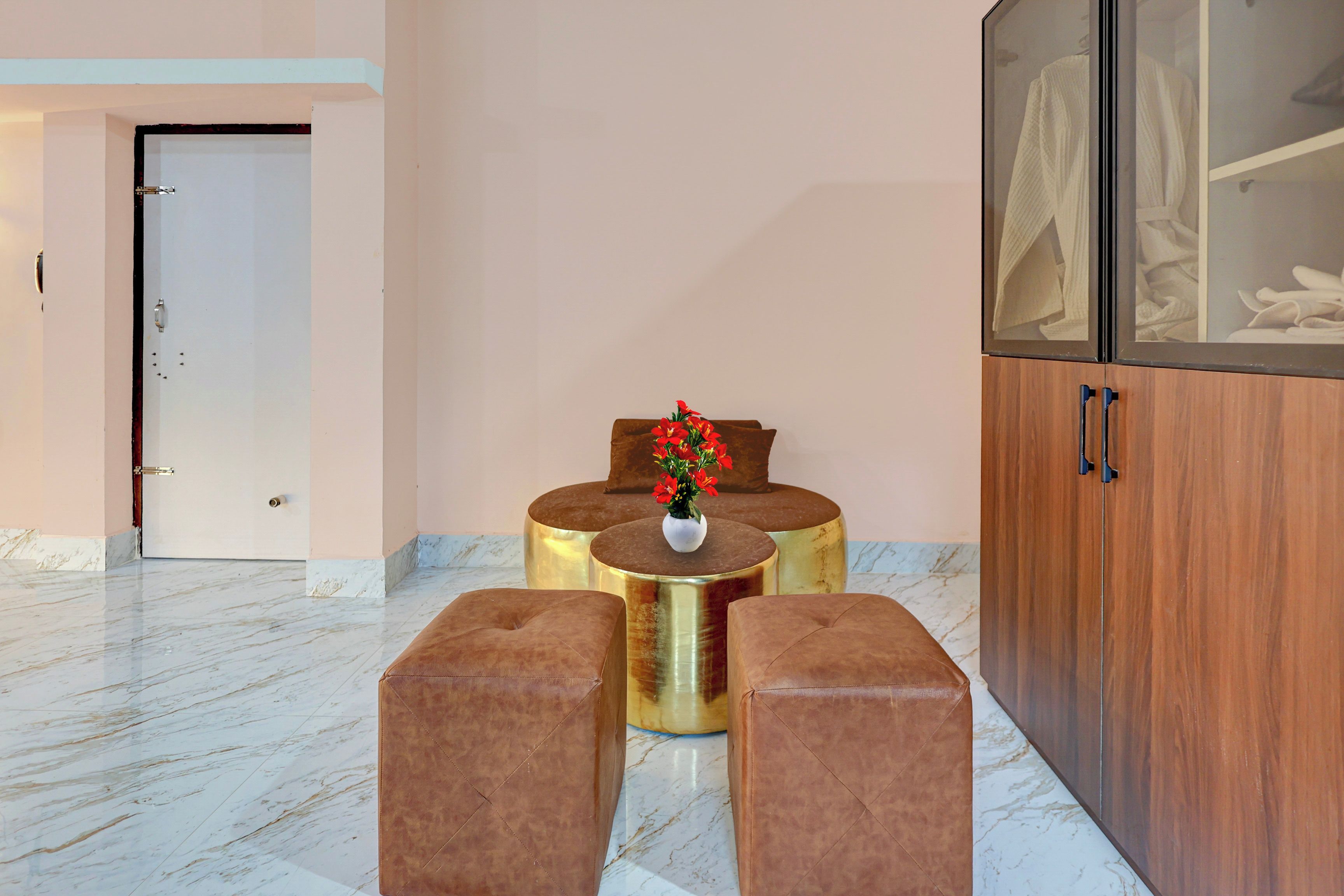 Un vestíbulo de hotel con piso de mármol, un aparador de madera con puertas de cristal y un área de descanso con un jarrón de flores rojas.