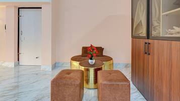 Un vestíbulo de hotel con piso de mármol, un aparador de madera con puertas de cristal y un área de descanso con un jarrón de flores rojas.