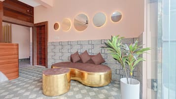 Un interior moderno con un sofá, dos mesitas doradas, una planta en maceta y una pared con espejos circulares.