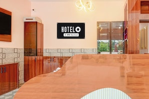 Interior de un hotel con una mesa de recepción, un cartel que indica que es OYO-Serviced y vistas al exterior a través de un ventanal.