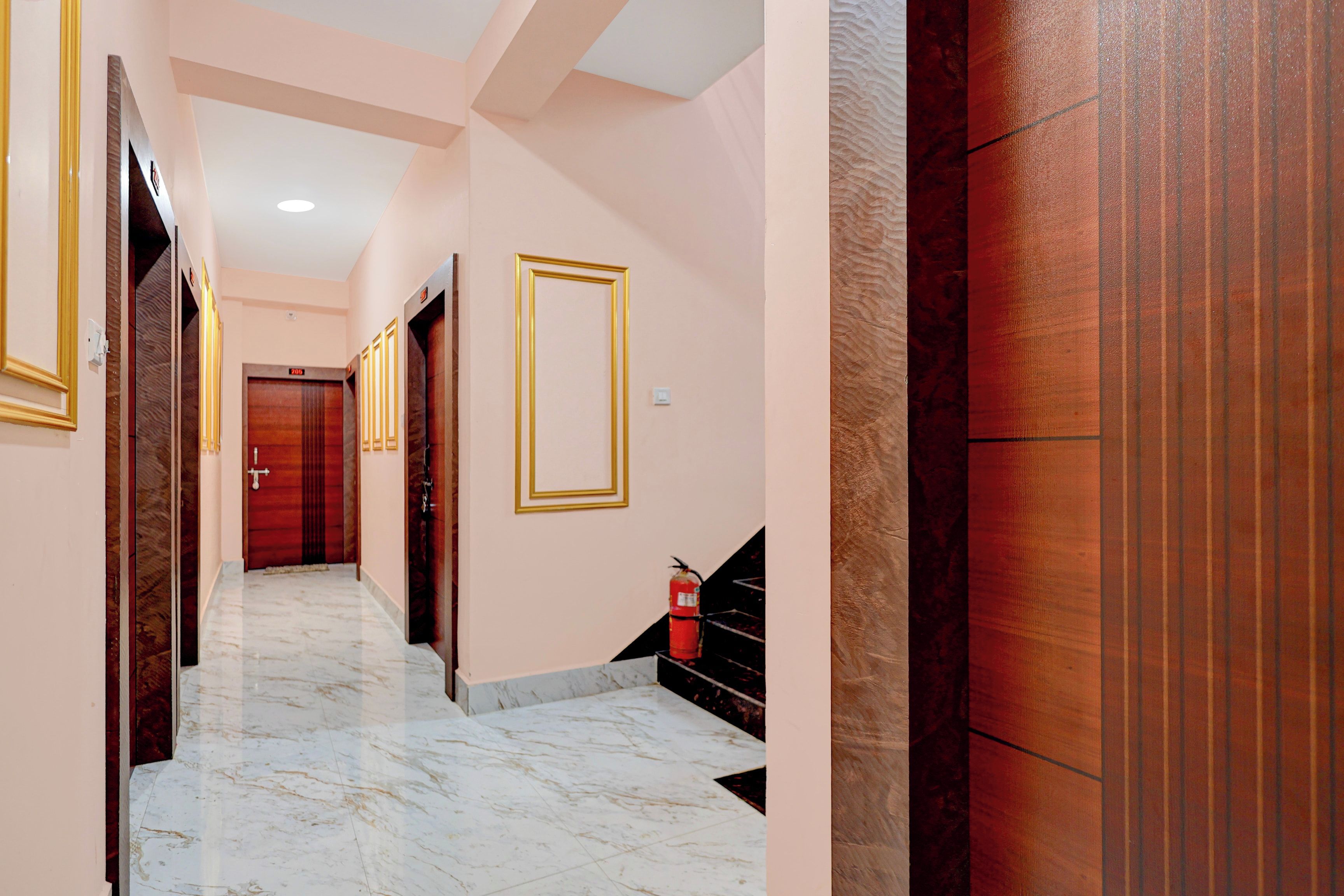 Un pasillo de hotel con suelo de mármol, puertas de madera con marcos dorados y un extintor en la pared.