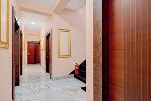 Un pasillo de hotel con suelo de mármol, puertas de madera con marcos dorados y un extintor en la pared.
