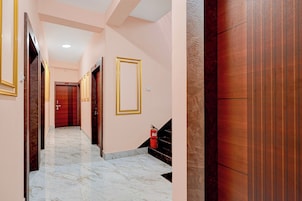Un pasillo de hotel con suelo de mármol, puertas de madera con marcos dorados y un extintor en la pared.