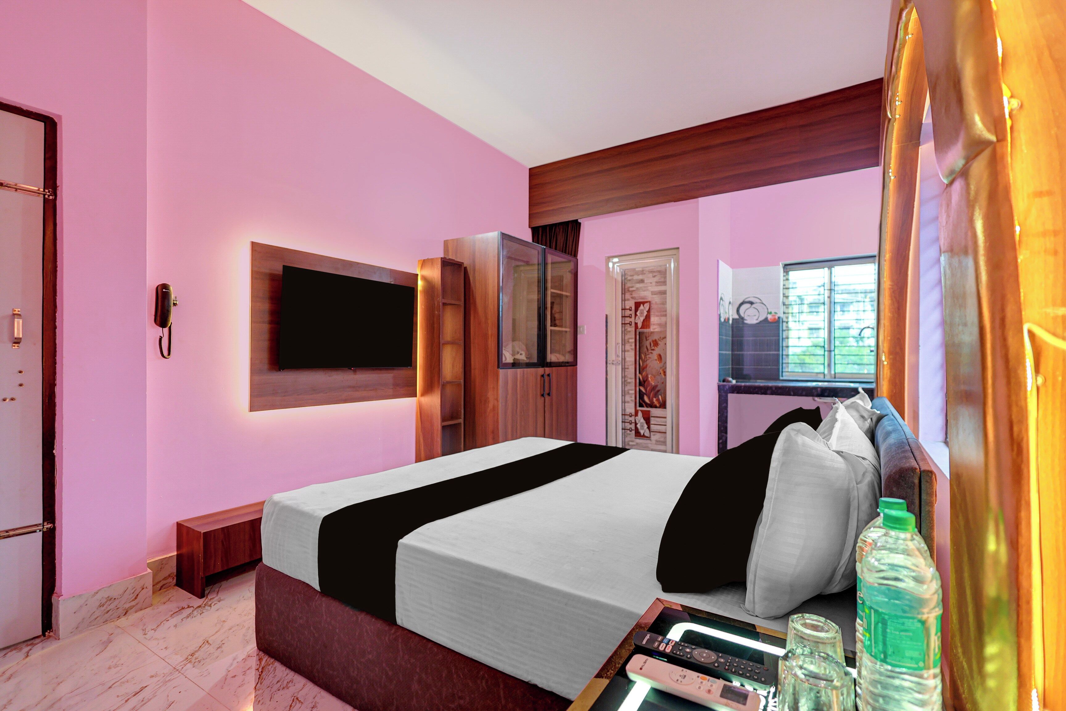 A modern bedroom with a large bed, a flat-screen TV mounted on the wall, and a window with a view of greenery.