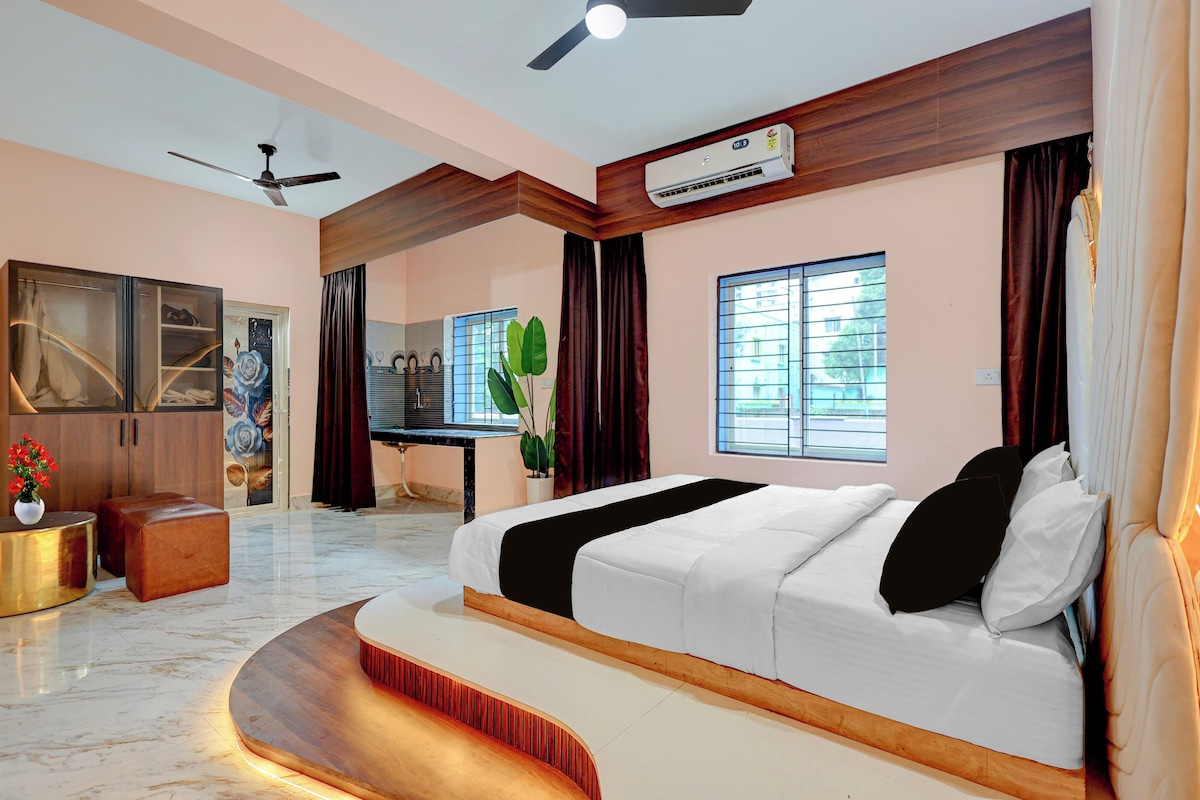 A modern bedroom with a large bed, a ceiling fan, an air conditioning unit, a vanity with a mirror, and a window with blinds.