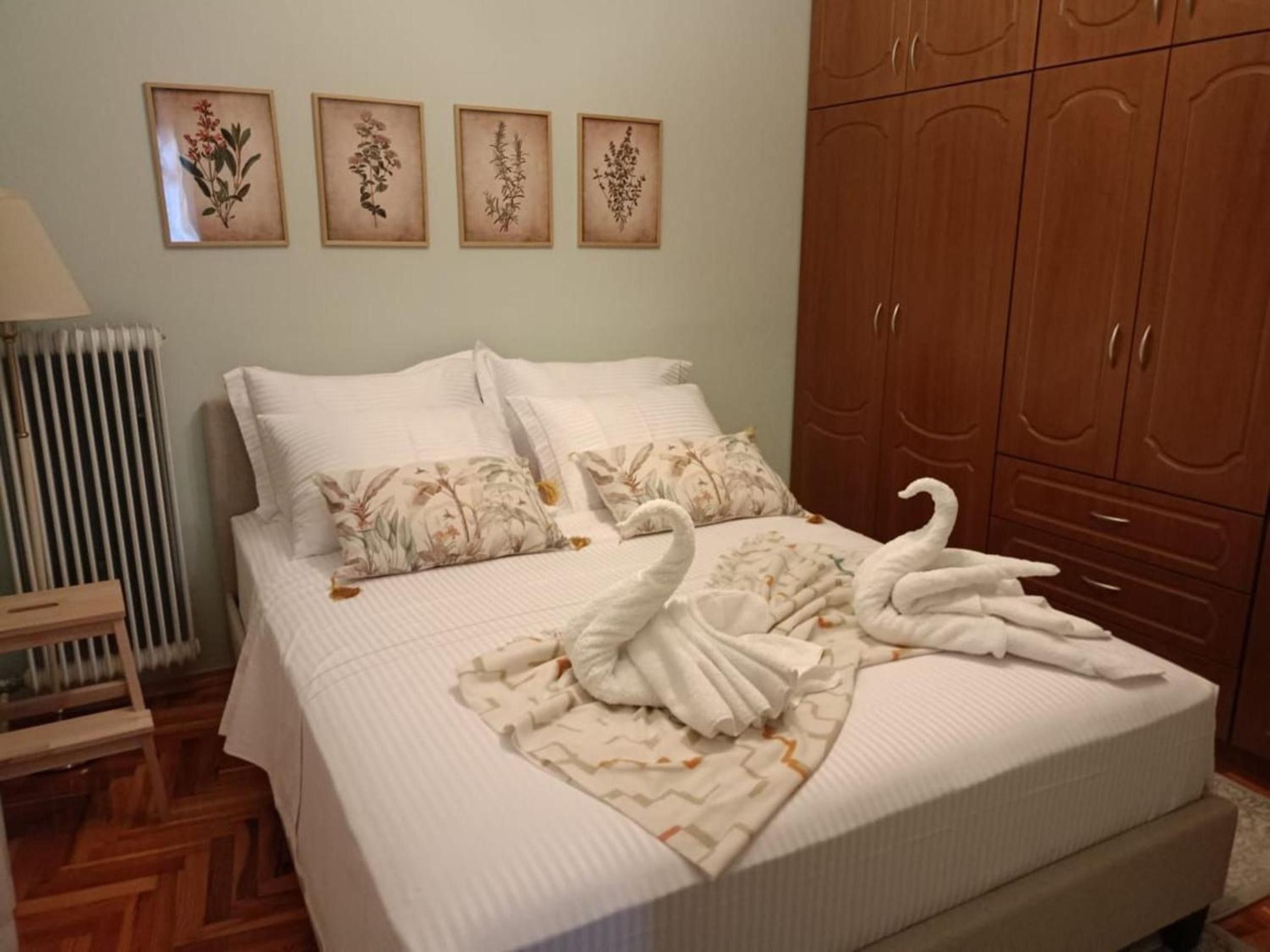 A bedroom with a bed, pillows, a radiator, a wooden wardrobe, and framed botanical prints on the wall.