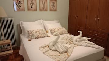 A bedroom with a bed, pillows, a radiator, a wooden wardrobe, and framed botanical prints on the wall.
