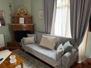 A living room with a grey sofa, a fireplace, a clock, and a framed rule poster.