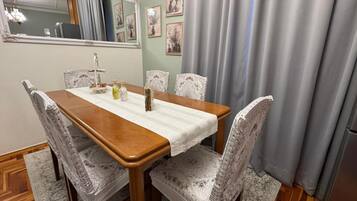 Un comedor con mesa de madera, sillas estampadas, una araña y un espejo en la pared.
