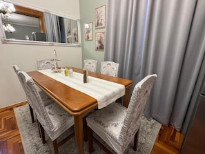 Ein Essbereich mit einem Holztisch, gemusterten Stühlen, einer Chandelieber und einem Spiegel an der Wand.