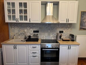 Eine Küche mit weißen Schränken, einem Edelstahlbackofen, einer Spüle mit Armatur und Fliesen mit Muster.