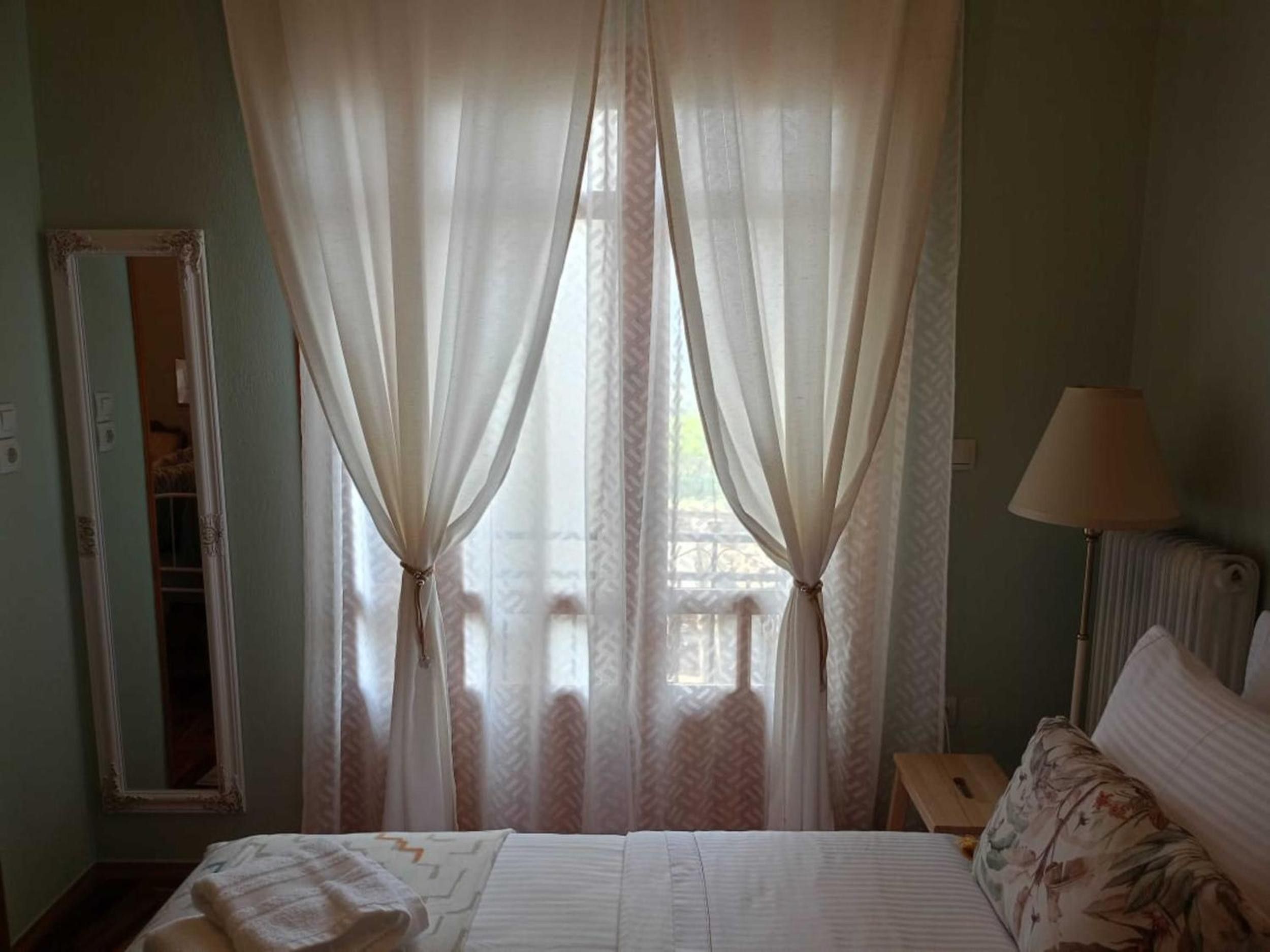 Un dormitorio con cama, mesita de noche, lámpara y cortinas traslúcidas.