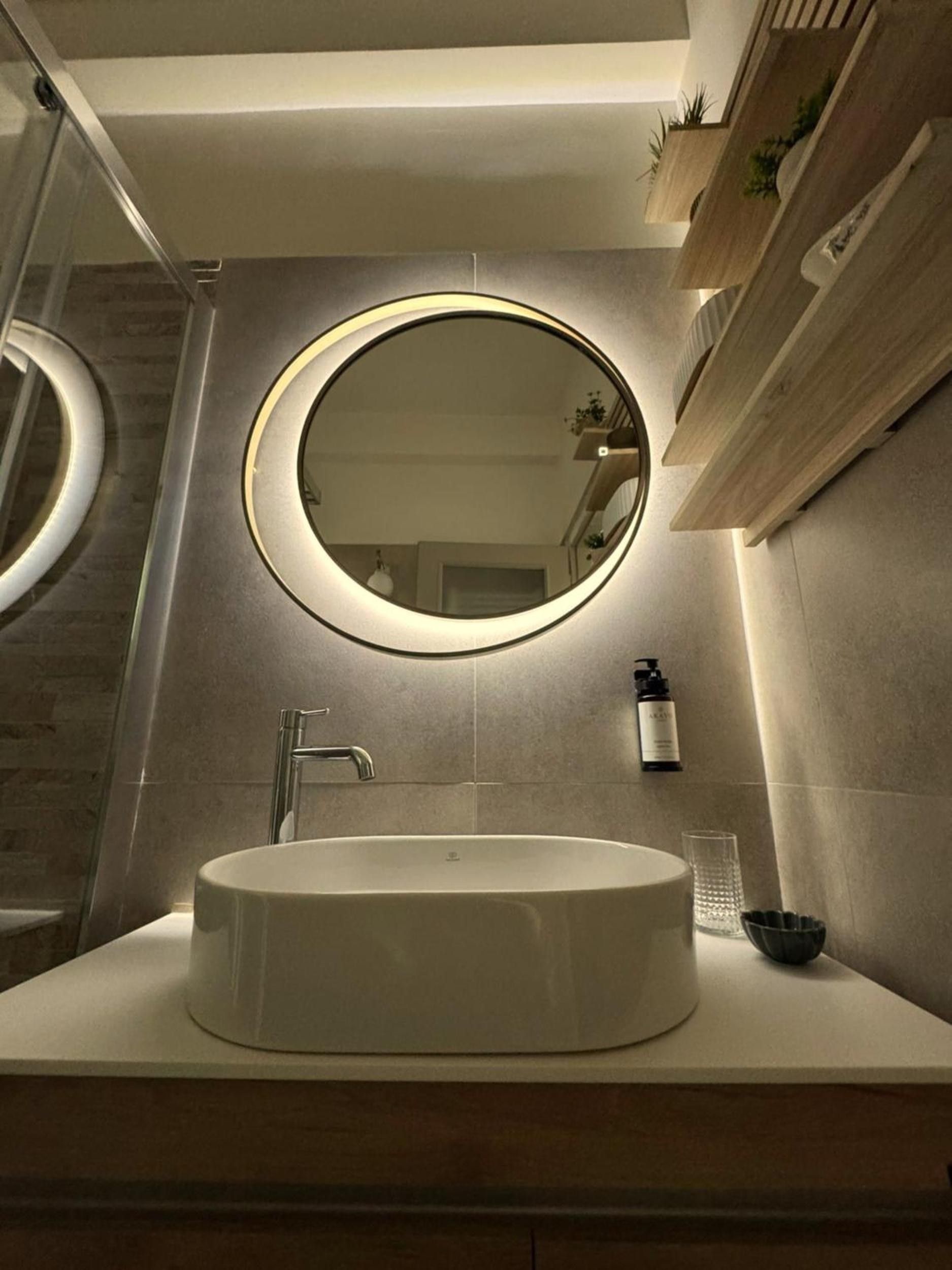 Een badkamer met een ronde spiegel, een witte wastafel en een douchehoek.