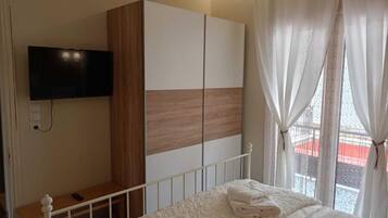 Un dormitorio con cama, televisor montado en la pared, armario y ventana con cortinas.