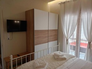 A bedroom with a bed, a TV mounted on the wall, a wardrobe, and a window with curtains.