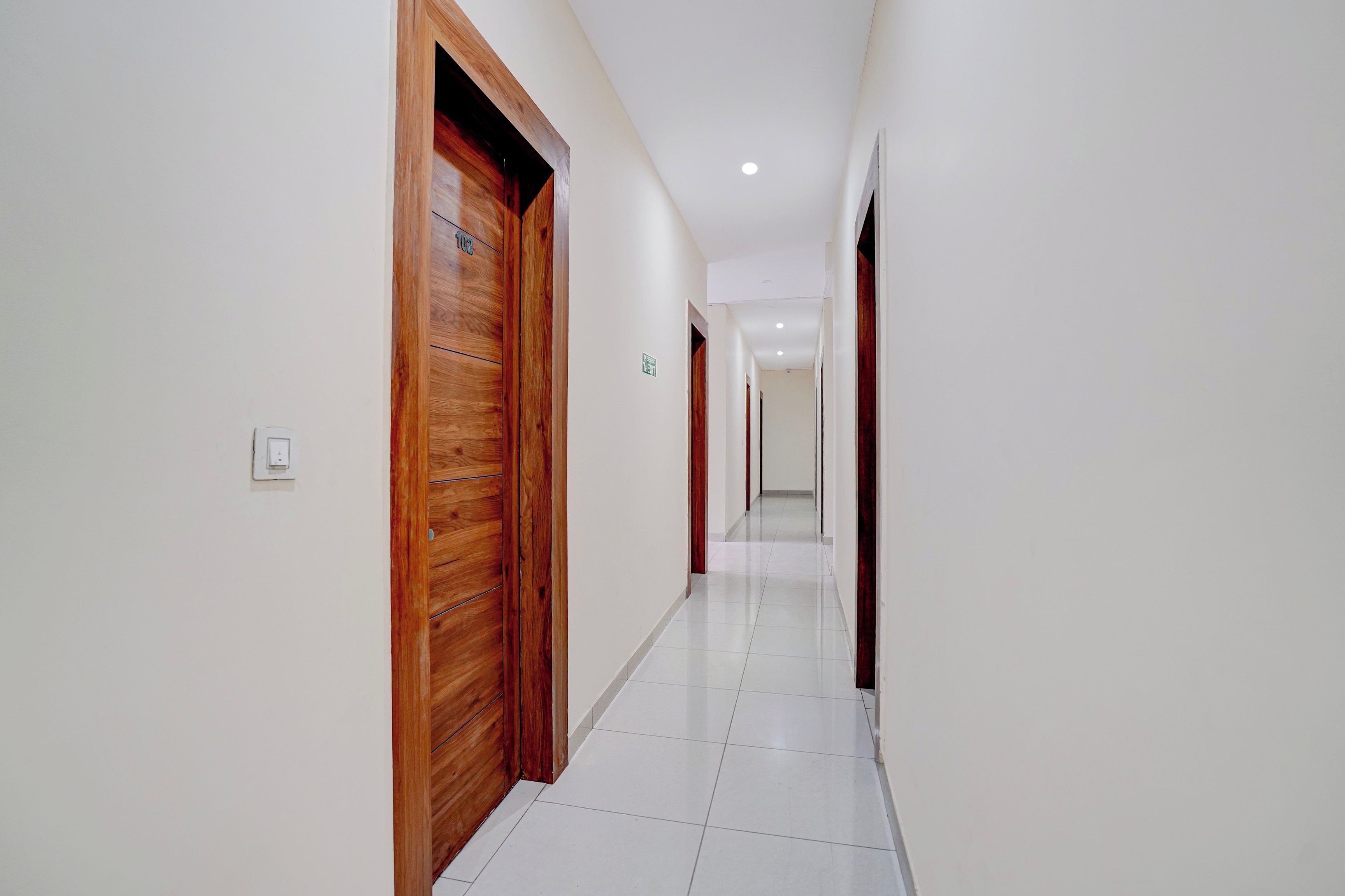 A corridor with wooden doors, white walls, and a tiled floor.