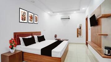 A modern hotel room with a wooden bed, a bedside table, a TV, and a coffee machine.