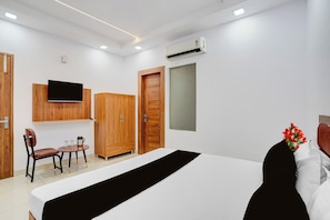 Une chambre d’hôtel comprenant un lit, un téléviseur fixé au mur, une armoire en bois, une petite table avec une chaise et une fenêtre donnant sur un paysage agréable.