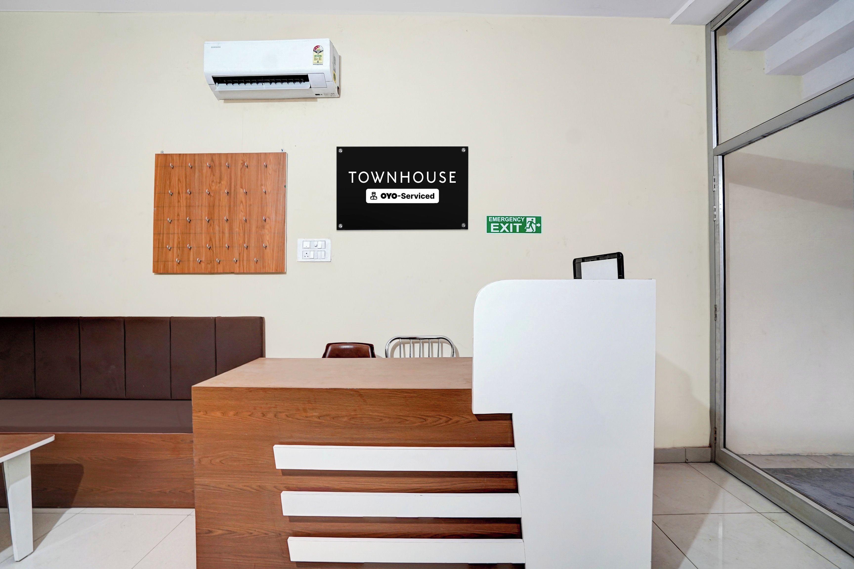A reception area with a wooden reception desk, a brown couch, a white chair, and an air conditioning unit mounted on the wall.