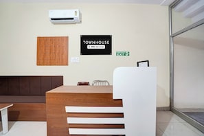 Un área de recepción con un mostrador de madera, un sofá marrón, una silla blanca y una unidad de aire acondicionado en la pared.