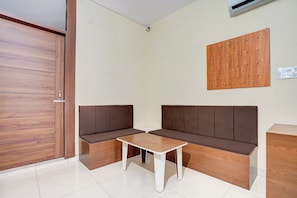 Une pièce avec une porte en bois, un sol carrelé de carreaux blancs, un canapé marron avec une table blanche, et un panneau en bois sur le mur.