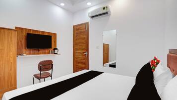 A hotel room with a bed, a wooden wardrobe, a television mounted on the wall, a mirror, and a small chair.