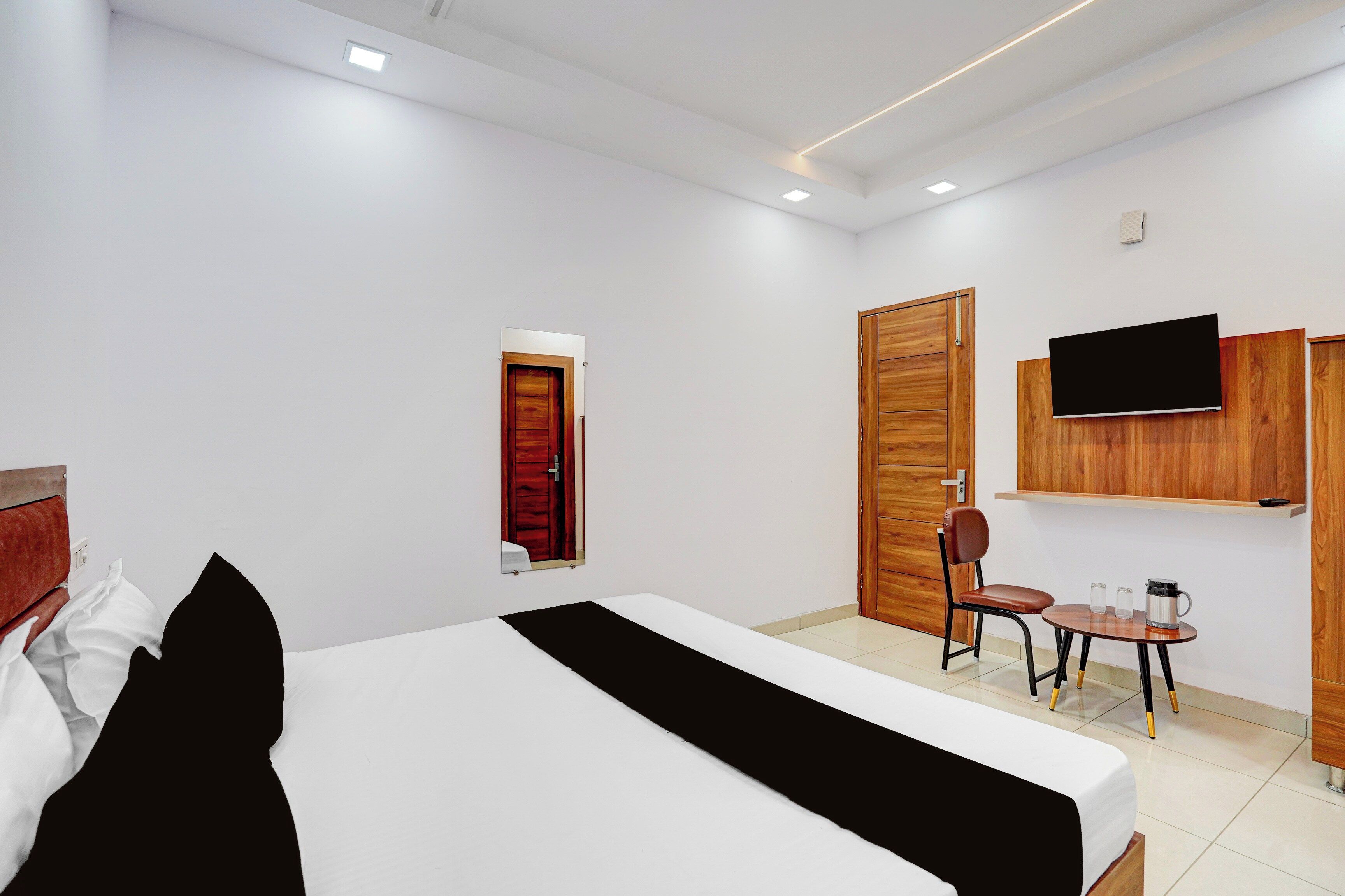 A hotel room with a bed, a desk with a chair, a television mounted on the wall, and a wooden wardrobe.